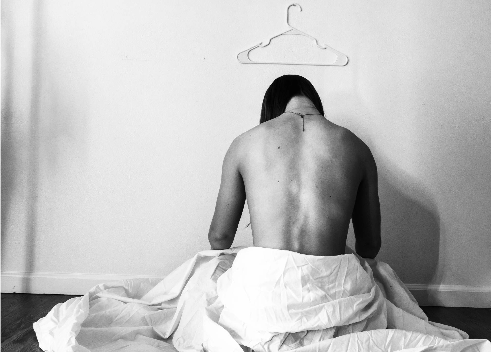 Black and white photograph of young person's back who is facing wall with coat hanger mounted on wall above them